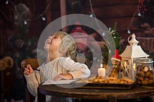 Cute toddler child, boy on Christmas, writing letter to Santa Claus and eating cookies at home, wooden cottage