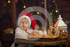 Cute toddler child, boy on Christmas, writing letter to Santa Claus and eating cookies at home, wooden cottage