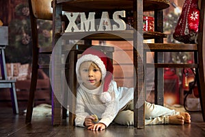 Cute toddler child, boy on Christmas, writing letter to Santa Claus and eating cookies at home, wooden cottage