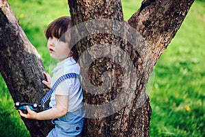 Cute toddler child boy with long hair in stylish outfit playing with toy car on the walk in summer