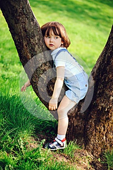 cute toddler child boy with long hair in stylish outfit playing with toy car on the walk in summer or spring garden