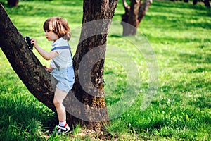 Cute toddler child boy with long hair in stylish outfit playing with toy car on the walk in summer