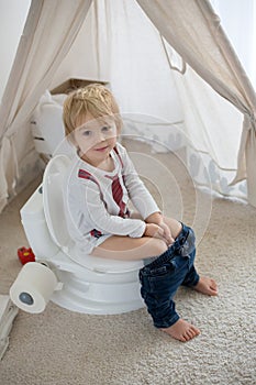 Cute toddler child, boy, sitting on a baby toilet potty, playing photo