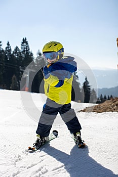 Cute toddler child in colorful ski wear, skiing in Italy on a sunny day, kids and adults skiing together