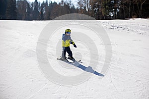 Cute toddler child in colorful ski wear, skiing in Italy on a sunny day, kids and adults skiing together