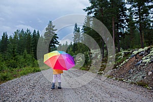 Cute toddler child with colorful umbrella, playing in the forest on a rainy day
