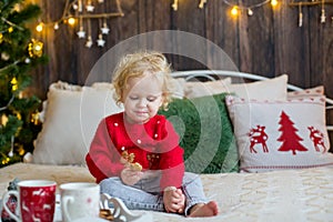 Cute toddler child, curly blond girl in a Christmas outfit, playing in a wooden cabin on Christmas, decoration around her. Child