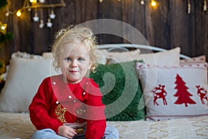 Cute toddler child, curly blond girl in a Christmas outfit, playing in a wooden cabin on Christmas, decoration around her. Child