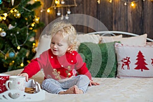 Cute toddler child, curly blond girl in a Christmas outfit, playing in a wooden cabin on Christmas, decoration around her. Child