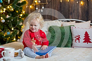 Cute toddler child, curly blond girl in a Christmas outfit, playing in a wooden cabin on Christmas, decoration around her. Child