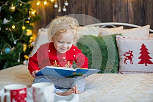 Cute toddler child, curly blond girl in a Christmas outfit, playing in a wooden cabin on Christmas, decoration around her. Child