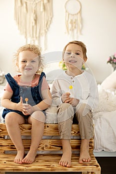 Cute toddler children, boy and girl, eating lolly pop at home