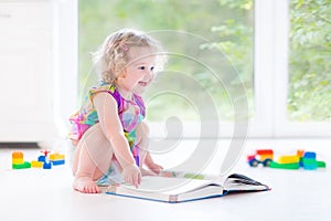 Cute toddler girl with blond curly hair reading book