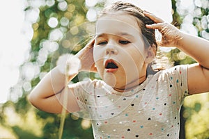 Cute toddler girl blows on dandelion, close up portrait in sunny summer day