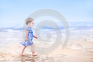 Cute toddler girl in blue dress walking on beach