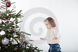 Cute toddler girl carefully walking around the Christmas tree