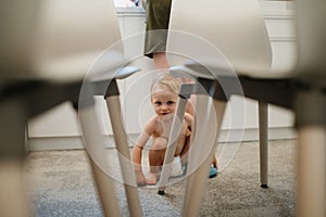 Cute toddler girl crawling takes first step, trying to stand up at home in kitchen with mother at background