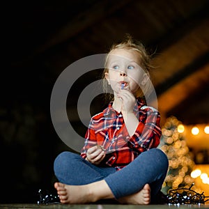 Cute toddler girl eating chocolate egg sitting in a hunting house decorated for Christmas. The concept of a Christmas morning.