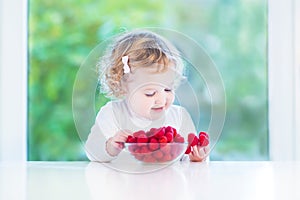 Cute toddler girl eating raspberries in a dining room with a big