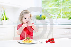 Cute toddler girl eating spaghetti in a white kitchen