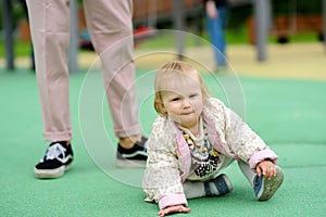 Cute toddler girl having fun on outdoor playground. Young father is teaching his little daughter to walk. First step of baby.