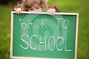 Cute toddler girl hiding behind a back to school blackboard