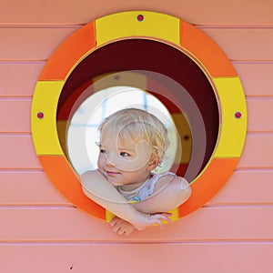 Cute toddler girl hiding in playhouse at playground