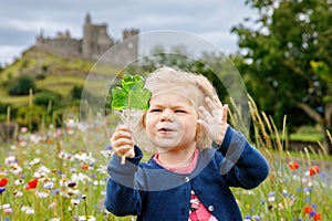 Cute toddler girl with Irish cloverleaf lollipop with Rock of Cashel castle on background. Happy healthy child on flower