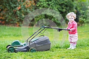 Cute toddler girl with a lawnmower in the garden