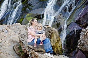 Cute toddler girl and mother sitting near water cascade of Powerscourt Waterfall, the highest waterfall in Ireland in co