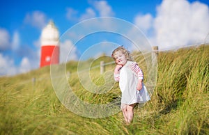 Cute toddler girl next to red lightshouse on beach photo