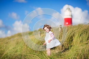 Cute toddler girl next to a red lightshouse on a beach photo