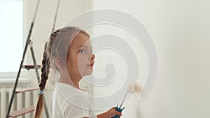 Cute toddler girl painting the wall with white color in new house. Family repair apartment home.