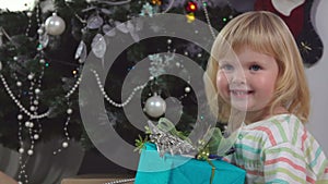 Cute toddler girl in pajama is holding her gift box in the Christmas morning