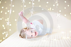 Cute toddler girl playing on a bed between warm soft Christmas l