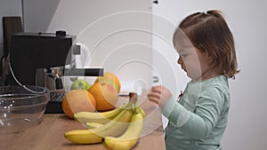Cute toddler girl playing with fruits at home on the kitchen. Independent pretend play