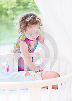 Cute toddler girl playing with newborn baby brother