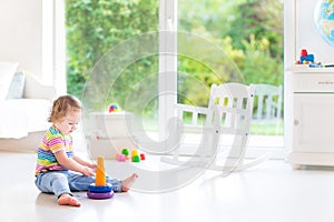 Cute toddler girl playing with a pyramid toy in a white room