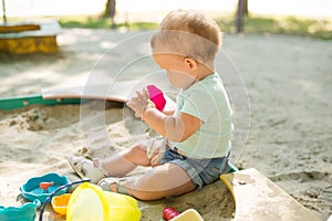 Cute toddler girl playing in sand on outdoor playground. Beautiful baby having fun on sunny warm summer day. Child with colorful