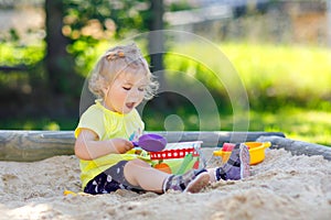 Cute toddler girl playing in sand on outdoor playground. Beautiful baby having fun on sunny warm summer sunny day. Happy