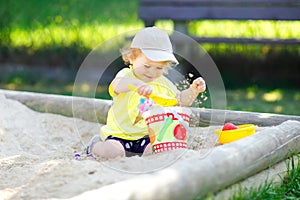 Cute toddler girl playing in sand on outdoor playground. Beautiful baby having fun on sunny warm summer sunny day. Happy