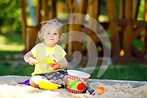 Cute toddler girl playing in sand on outdoor playground. Beautiful baby having fun on sunny warm summer sunny day. Happy