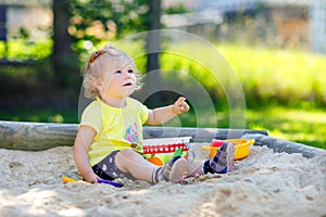 Cute toddler girl playing in sand on outdoor playground. Beautiful baby having fun on sunny warm summer sunny day. Happy