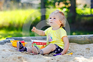 Cute toddler girl playing in sand on outdoor playground. Beautiful baby having fun on sunny warm summer sunny day. Happy