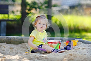 Cute toddler girl playing in sand on outdoor playground. Beautiful baby having fun on sunny warm summer sunny day. Happy