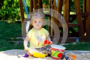 Cute toddler girl playing in sand on outdoor playground. Beautiful baby having fun on sunny warm summer sunny day. Happy