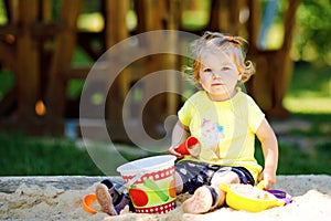 Cute toddler girl playing in sand on outdoor playground. Beautiful baby having fun on sunny warm summer sunny day. Happy