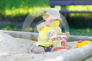 Cute toddler girl playing in sand on outdoor playground. Beautiful baby having fun on sunny warm summer sunny day. Happy