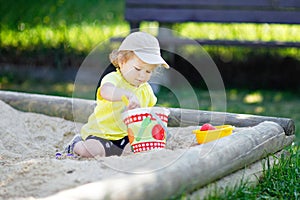 Cute toddler girl playing in sand on outdoor playground. Beautiful baby having fun on sunny warm summer sunny day. Happy