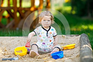 Cute toddler girl playing in sand on outdoor playground. Beautiful baby in red gum trousers having fun on sunny warm